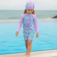 Niña usando ropa de baño de sirena para niñas de 2 piezas con diseño de escamas 3D, polo manga rangla y gorro de natación en la piscina.